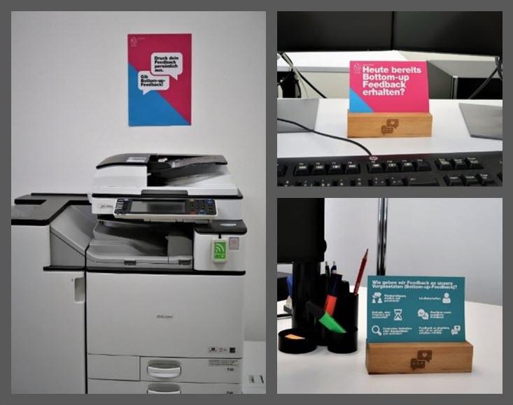 Auf der linken Hälfte ist ein Plakat oberhalb eines Druckers an der Wand angebracht. Oben rechts und unten rechts ist eine Postkarte in einem Schreibtisch in einem Holzhalter platziert