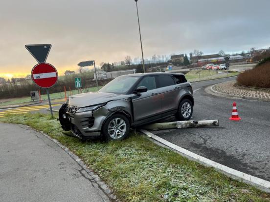 Das verunfallte Auto steht mit eingedrückter Front halbwegs im Wiesland des Kreisels. Unter dem Fahrzeug liegt der umgefahrene Kandelaber.