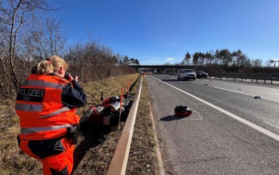 Eine Polizistin fotografiert das verunfallte Motorrad hinter der Autobahnleitplanke