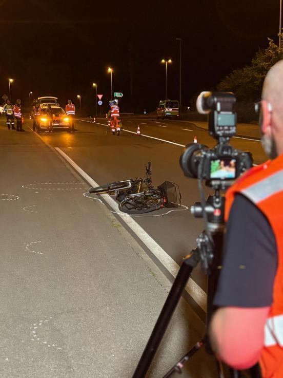 Polizist fotografiert auf der Strasse liegendes Velo, im Hintergrund mehrere Polizistinnen vor Polizeiauto