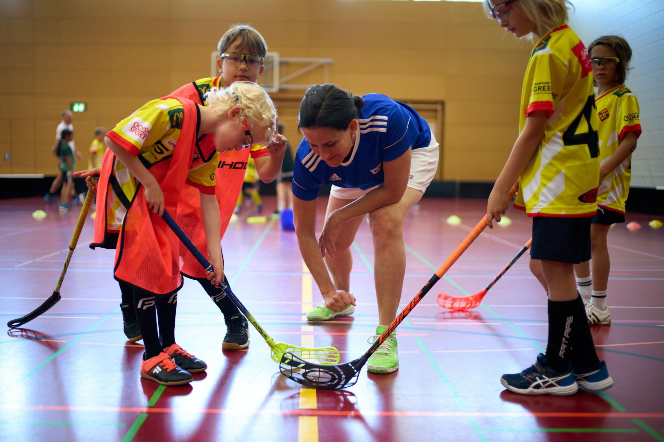 Eine Leiterin gibt einer Gruppe von Kindern Tipps im Unihockey Training