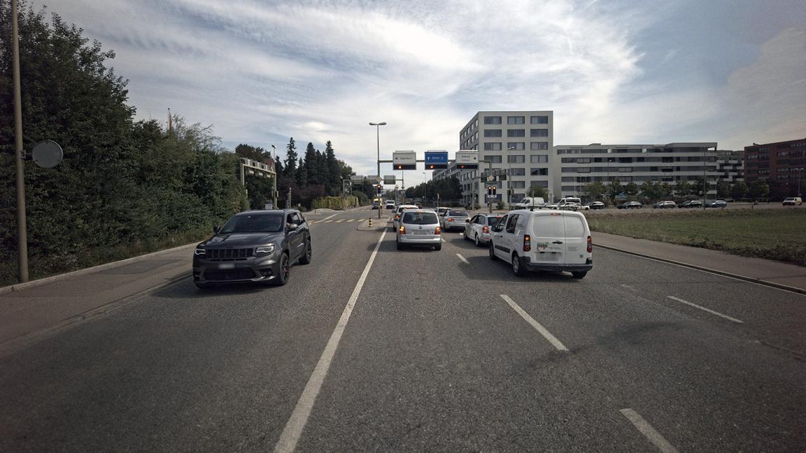 Eine Strasse mit mehreren Autos führt mehrspurig auf ein Licht-signal zu.