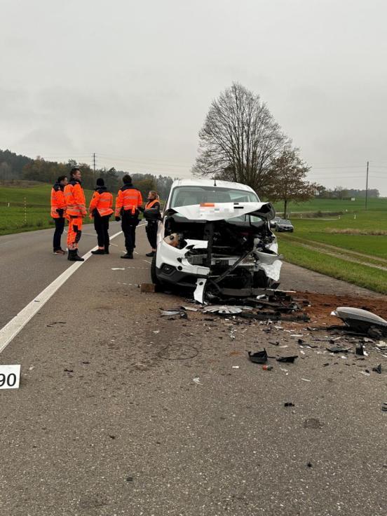 Polizisten stehen neben einem stark beschädigten Fahrzeug auf einer Strasse