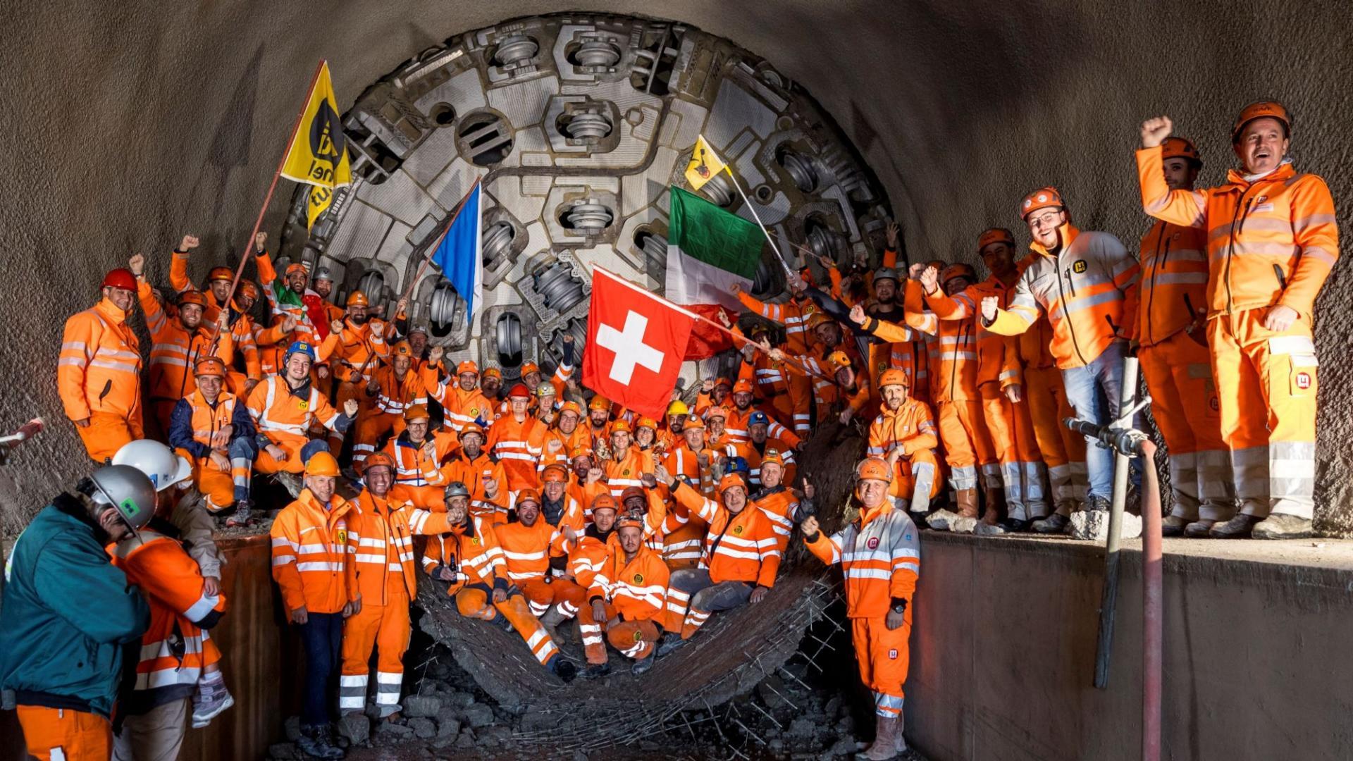 Eine Gruppe von Mineuren und Regierungsrat Martin Neukom feiern vor dem Bohrkopf den erfolgreichen Durchstich