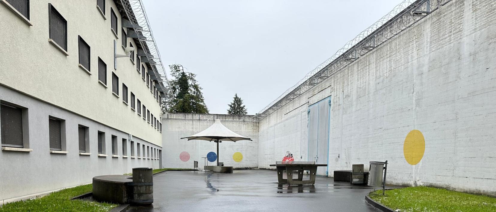 Der Spazierhof des ehemaligen Gefängnisses ist von Betonmauern umgeben und hat einen Pingpongtisch und Sonnenschirm sowie Rasenfläche in der Mitte.