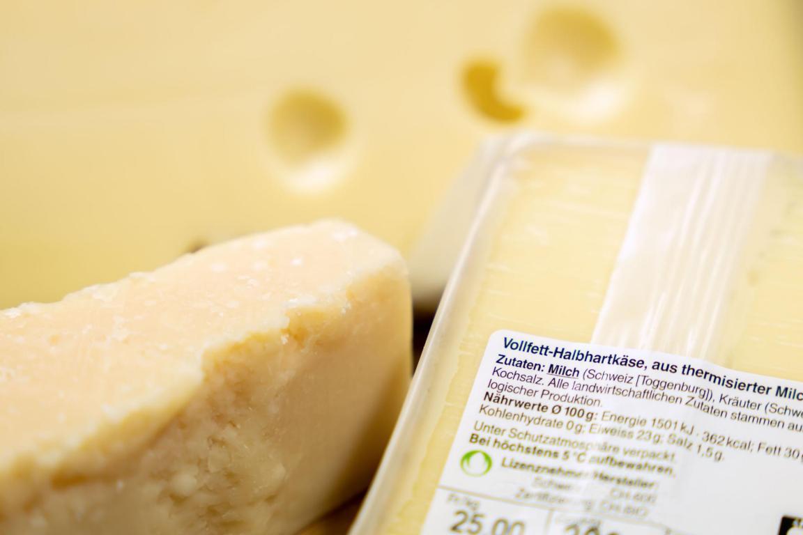 Das Foto zeigt verschiedene Käsesorten. Ein Stück Käse ist verpackt und die Etikette mit den Angaben zur Zusammensetzung ist abgebildet.