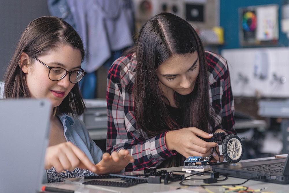 Zwei Schülerinnen bauen aus Einzelteilen einen Roboter zusammen.