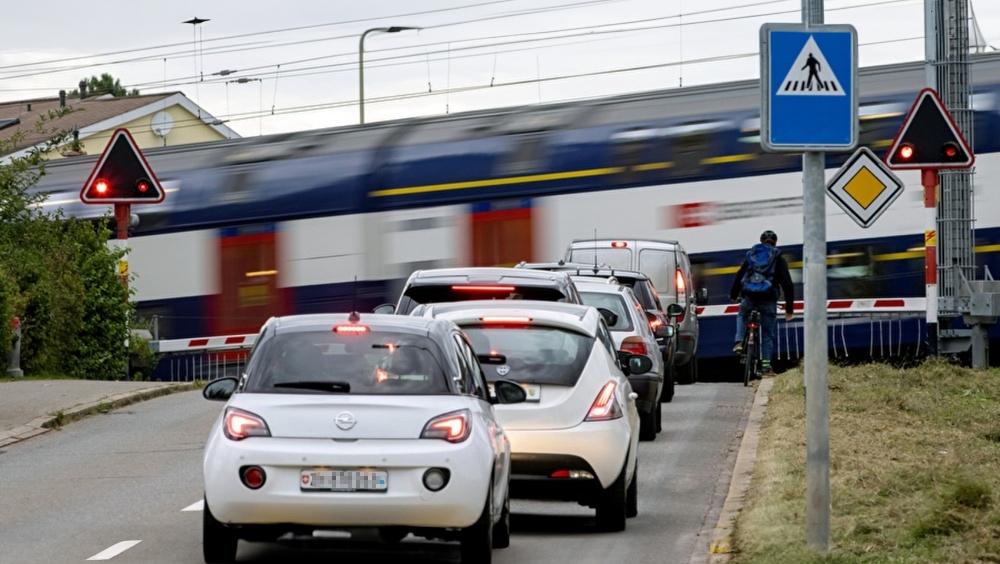 Mehrere Autos stehen vor einem geschlossenen Bahnübergang und ein Zug fährt durch.