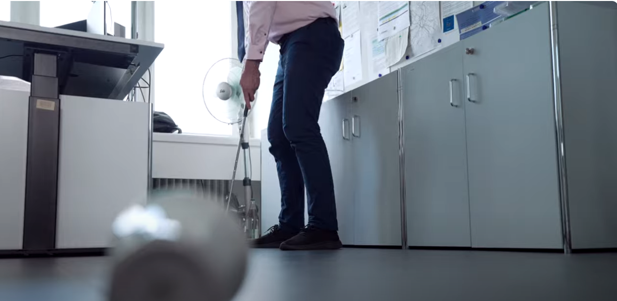 Mann spielt Golf in seinem Büro.