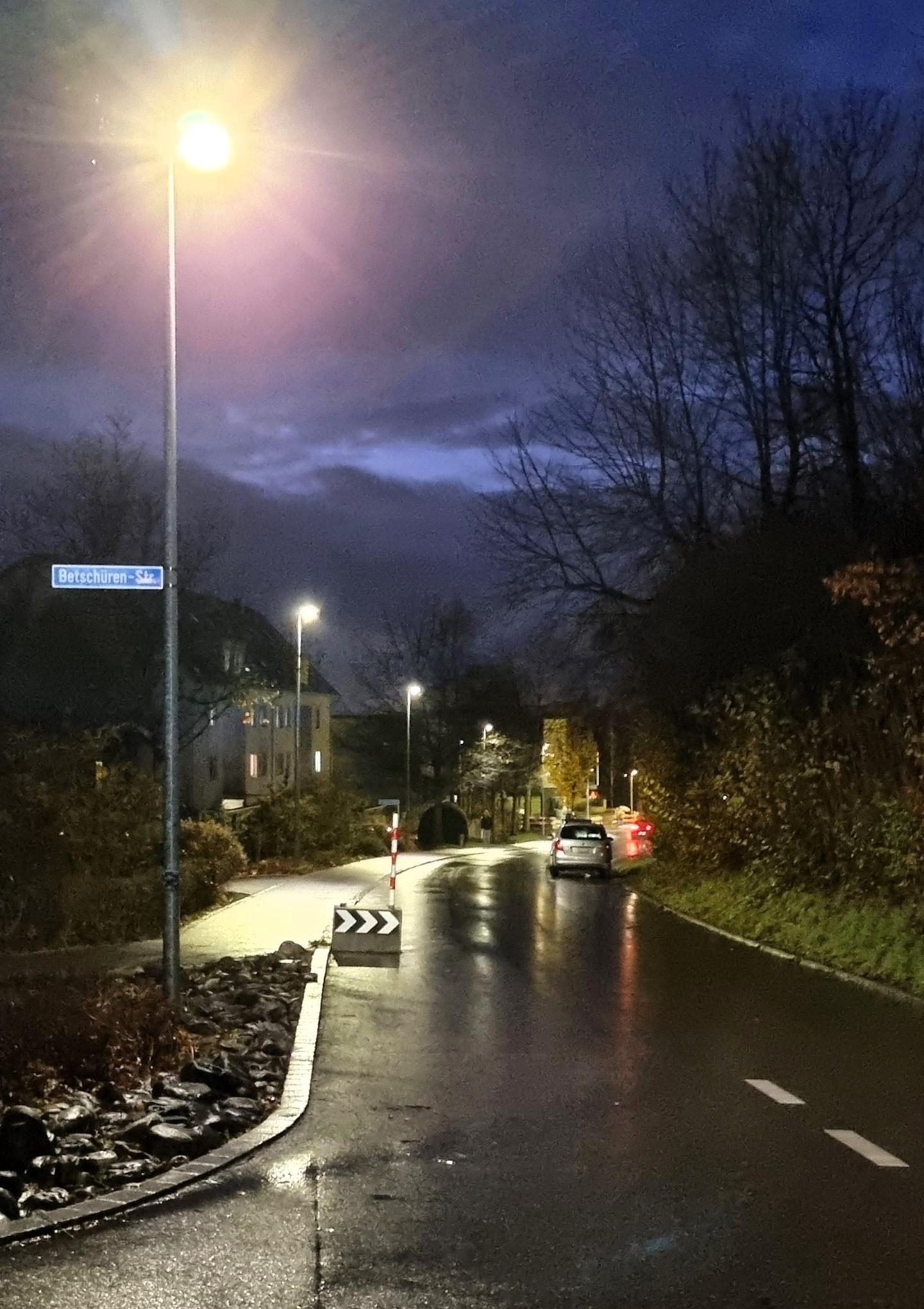 Eine Strasselaterne beleuchtet in dunkler Nacht eine regennasse Strasse. 