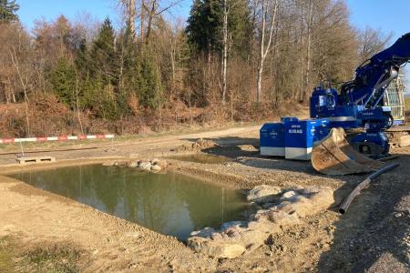 Bagger der einen rechteckigen Weiher, der bereits mit Wasser gefüllt ist, ausgehoben hat