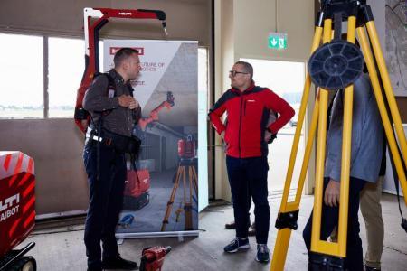 Zwei Mitarbeiter der Hilti Schweiz AG stehen nebeneinander. Einer hat den roten, tragbaren Gerätebalancer auf dem Rücken, der wie ein Rucksack angezogen werden kann und einen maschinellen Kranarm besitzt.