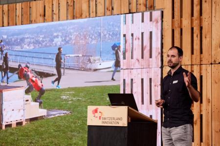 Marco Hutter steht auf der Bühne im Event Hangar vom Innovationspark Zürich  und  präsentiert den roten, vierbeinigen, autonomen Roboter ANYmal von ANYbotics