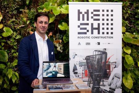 Ammar Mirjan, CEO von MESH Robotic Construction steht an seinem Stand und lächelt in die Kamera. 