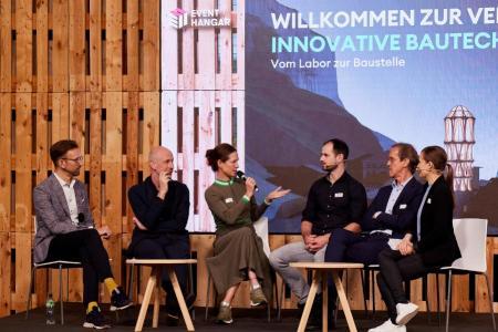 (v.l.n.r.) Markus Siemienik von der SBB, Benjamin Dillenburger von der ETH Zürich, Anita Eckardt von der Implenia AG, Marco Hutter von der ETH Zürich, Philip Leistner vom Fraunhofer-Institut für Bauphysik und Noémi Besedes, Moderatorin sitzen nebeneinander auf der Bühne in einer Podiumsdiskussion. 