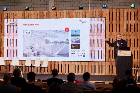 Martin Sturzenegger steht auf der Bühne des Event Hangar im Innovationspark Zürich und präsentiert den UZH Space Hub 